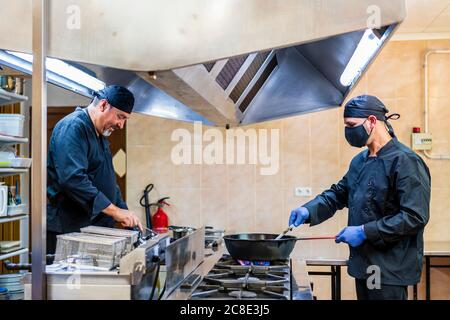 Traditionelle Küche in der Restaurantküche, Koch trägt Schutzmaske Stockfoto