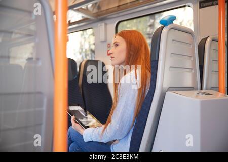 Nachdenkliche Frau hält digitales Tablet, während sie im Zug sitzt Stockfoto