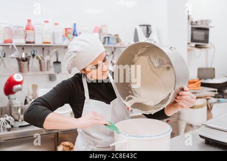 Weibliche Bäcker Leeren Teig in Behälter bei der Bäckerei Stockfoto