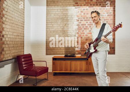 Senior Mann spielt Bass-Gitarre in einer Loft-Wohnung Stockfoto