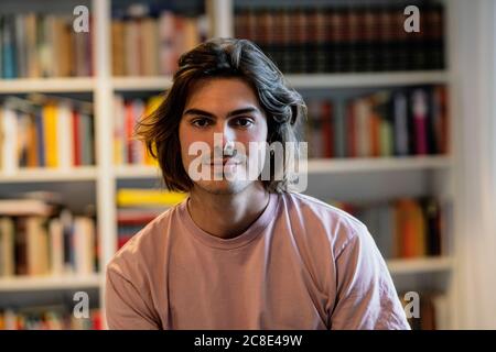 Nahaufnahme eines selbstbewussten männlichen Besitzers, der im Café gegen das Bücherregal sitzt Stockfoto