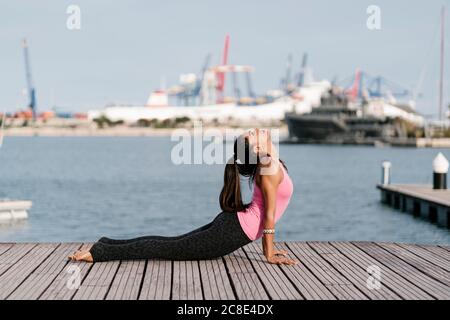 Frau übt Kobra Pose auf Pier gegen Meer am Hafen Stockfoto