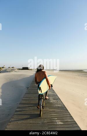Surfer mit dem Fahrrad während des Sonnenuntergangs, halten Surfbrett Stockfoto