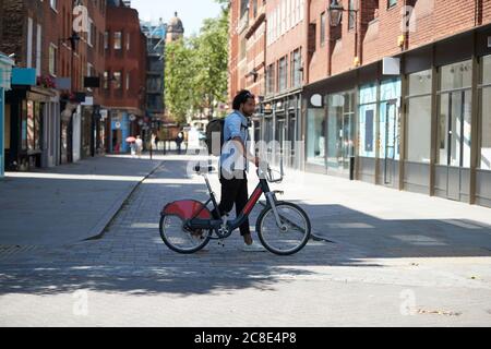 Junger Mann, der die Straße überquert, mit Leihfahrrad, London, Großbritannien Stockfoto
