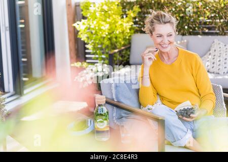 Portrait einer glücklichen reifen Frau, die auf der Terrasse sitzt und Heidelbeeren isst Stockfoto