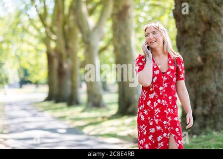 Frau, die über Smartphone spricht, während sie auf dem Fußweg läuft Öffentlicher Park Stockfoto