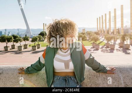 Nachdenkliche trendige Frau, die sich an einer Stützmauer in der Stadt lehnt Stockfoto