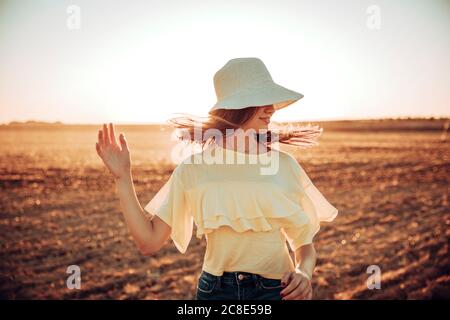 Junge Frau wirft Haare auf dem Feld gegen den Himmel während des Sonnenuntergangs Stockfoto