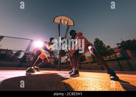 Männliche Freunde spielen Basketball auf dem Platz in der Nacht während des Wochenendes Stockfoto