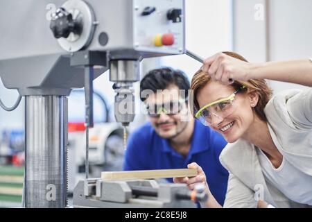 Weibliche Managerin, die Metall bohrt, während sie männliche Arbeiter in Metall austrainiert Branche Stockfoto