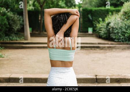 Athletische junge Frau, die die Arme im Park streckt Stockfoto