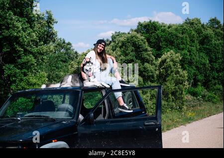 Lächelnde Frau, die an sonnigen Tagen mit Hund auf dem Dach sitzt Stockfoto