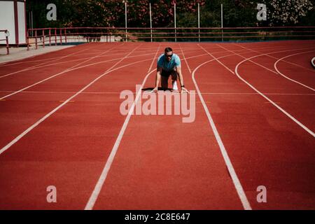 Männlicher Athlet in Startposition auf der Tartanbahn Stockfoto