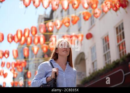 Nachdenkliche junge Frau, die in der Stadt unter chinesischen Laternen läuft Stockfoto