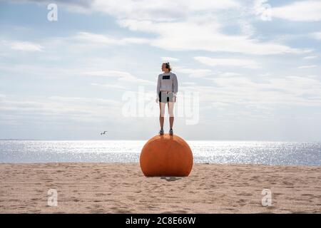 Junge Frau, die am Strand auf orangefarbenem Stein steht Stockfoto