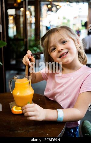 Nahaufnahme eines lächelnden Mädchens mit Orangensaft auf dem Tisch stehend Im Café Stockfoto