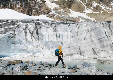 Männlicher Wanderer, der den schmelzenden Gletscher erkundet, während er auf Felsen steht Stockfoto