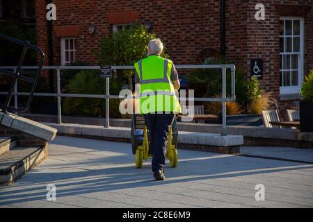 Ein Arbeiter in einer Hi-Vis- oder Sichtjacke, der einen Sackkarre auf die Straße schiebt Stockfoto