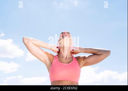 Fröhliche sportliche Frau trägt Kopftuch, während sie gegen den blauen Himmel steht Stockfoto