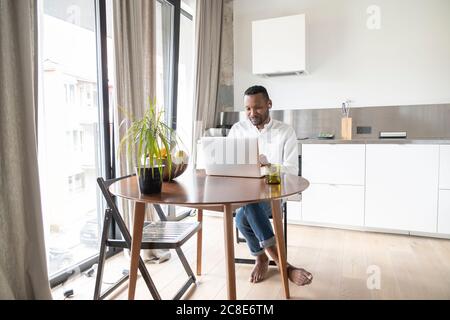 Portrait des Mannes am Tisch sitzen in modernen Wohnung mit Laptop und Kopfhörer Stockfoto