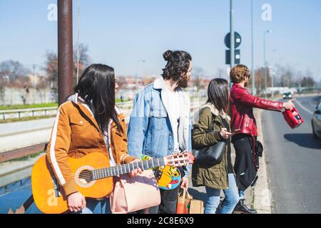 Junger Mann, der mit Freunden auf der Straße steht, beim Trampen Stadt an sonnigen Tagen Stockfoto