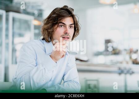 Nachdenklicher männlicher Profi, der Kaffee trinkt, während er im Café sitzt Stockfoto