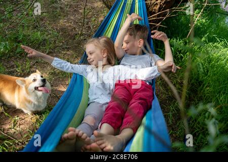 Nette Freunde, die Hund beim Entspannen in der Hängematte suchen Wald Stockfoto
