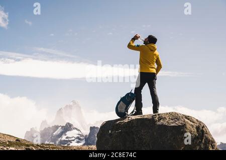 Männlicher Wanderer, der Wasser trinkt, während er auf Felsen gegen Himmel steht, Patagonien, Argentinien Stockfoto