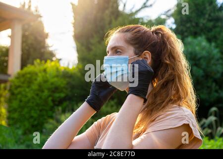 Nahaufnahme einer jungen Frau, die Maske und Handschuhe trägt und wegschaut Im Hof Stockfoto