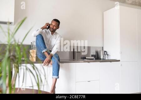 Porträt eines ernsthaften Mannes am Telefon, der in der Küche sitzt Zähler zu Hause mit Blick auf die Ferne Stockfoto