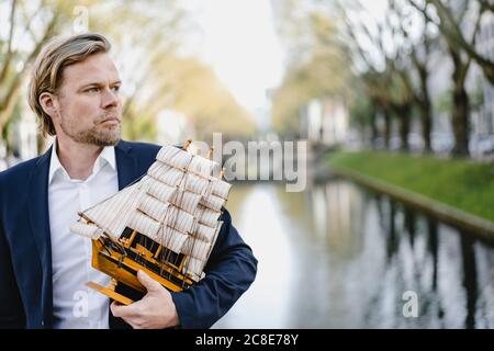 Geschäftsmann hält Modellschiff an einem Kanal Stockfoto