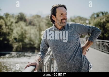 Lächelnder reifer Mann schaut weg, während er auf dem Steg steht parken Stockfoto