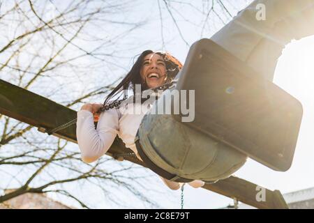 Fröhliche junge Frau schwingt gegen den Himmel im Park während der Sonne Tag Stockfoto