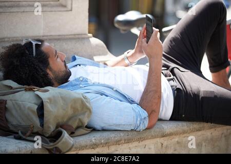 Junger Mann, der sich in der Stadt entspannt, mit Blick auf das Handy, London, Großbritannien Stockfoto