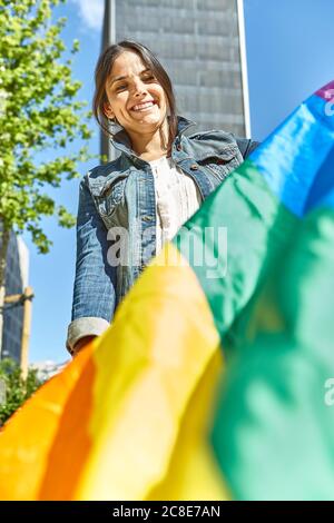 Glückliche Frau hält Regenbogenfahne in der Stadt Stockfoto