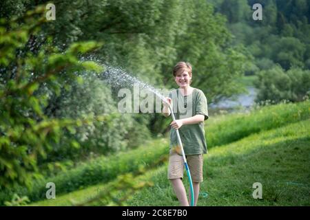 Lächelnder Junge, der Wasser mit Schlauch im Wald sprüht Stockfoto