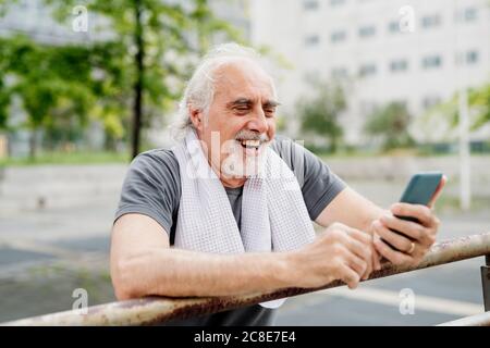 Nahaufnahme eines fröhlichen älteren Mannes mit Smartphone im Stehen Durch Geländer Stockfoto