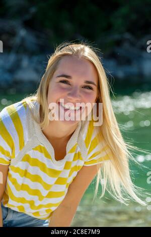 Lächelnde junge Frau mit blonden Haaren, die gegen den Fluss stehen Stockfoto