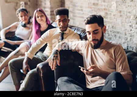 Gruppe von Freunden sitzen auf dem Sofa in einem Loft mit Smartphone Stockfoto