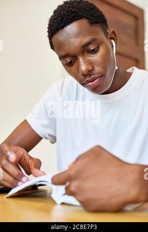 Nahaufnahme eines jungen Mannes, der beim Lesen von Büchern Musik hört Tisch zu Hause Stockfoto