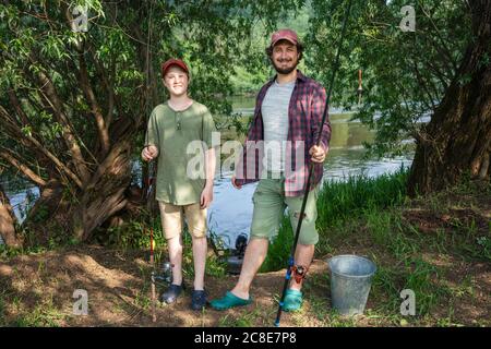 Vater und Sohn halten Angelruten, während sie am Flussufer stehen