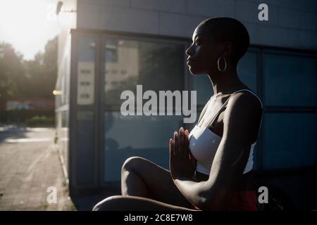 Junge Frau meditiert, während sie draußen in der Stadt bei Sonnenschein sitzt Tag Stockfoto
