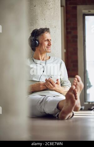 Älterer Mann mit Kopfhörern, der Musik in einer Loft-Wohnung hört Stockfoto