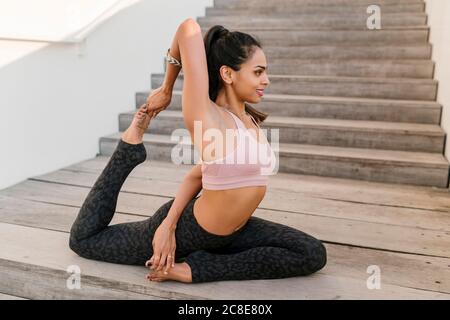 Weibliche Athletin übt einbeinige Königstaube Pose auf Holztreppen Stockfoto