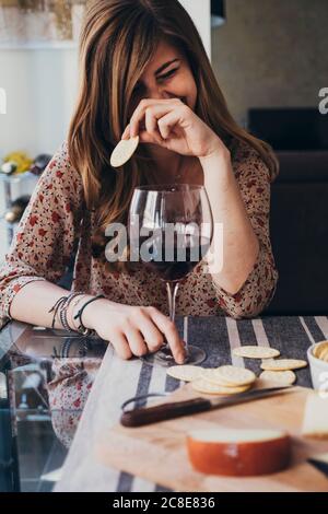 Fröhliche junge Frau, die Cracker hält, während sie am Esstisch sitzt Stockfoto