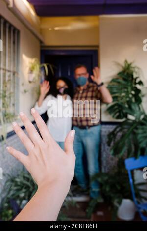 Beschnittene Hand des Nachbarn winkt zu Paar stehen im Hof Stockfoto