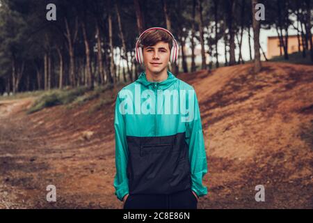 Teenager mit Kopfhörern im Regenmantel im Wald Stockfoto