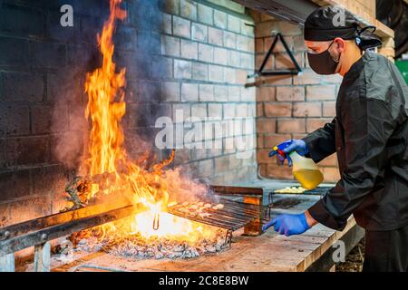 Traditionelle Küche von Meeresfrüchten auf dem Grill in der Restaurantküche, Koch trägt Schutzmaske Stockfoto