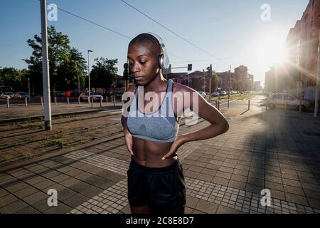 Sportlerin, die Musik über Kopfhörer hört, während sie auf der Straße steht In der Stadt während des sonnigen Tages Stockfoto