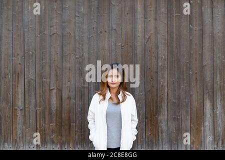 Junge schöne asiatische Frau steht gegen Holzwand Stockfoto